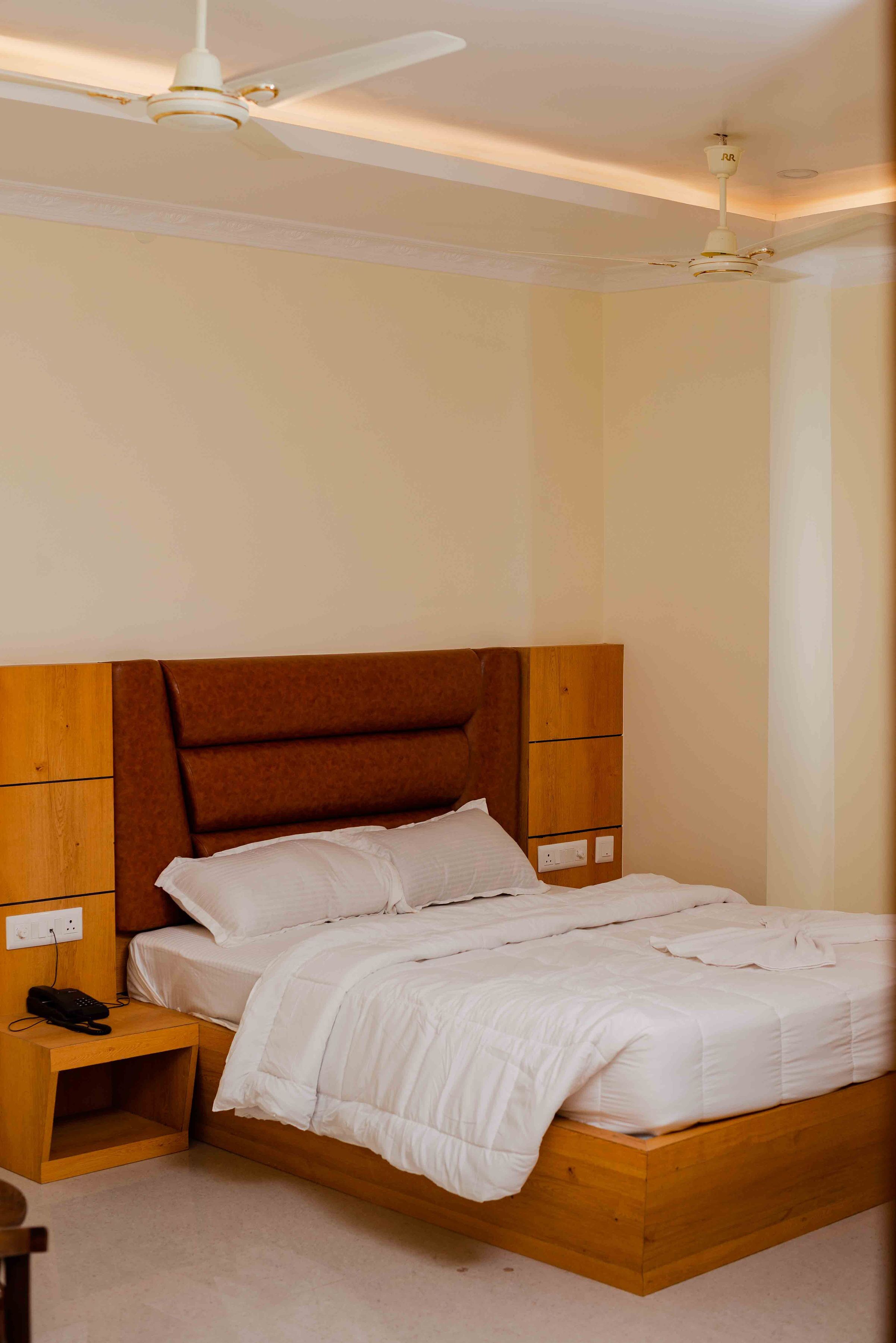 A bedroom with a wooden bed, white bedding, a nightstand with a phone, and a ceiling fan.