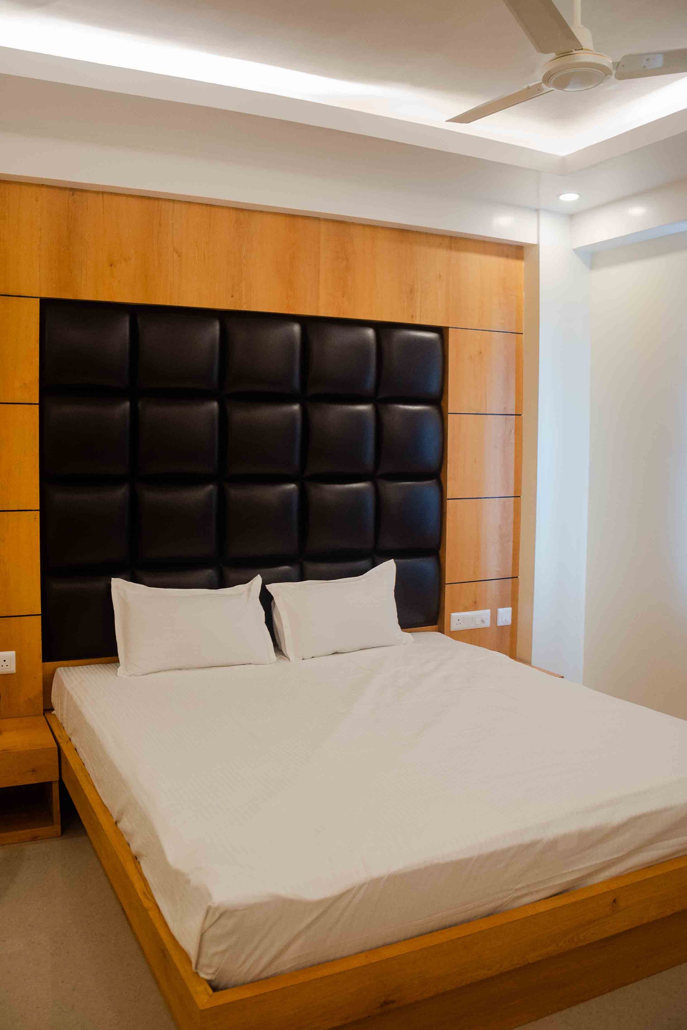 A modern bedroom with a wooden headboard, a bed with white linens, and a ceiling fan.