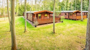 A row of wooden cabins with balconies, surrounded by a grassy area and trees. - Luxury log cabin with veranda nestled in Kenwick Park, Louth (Louth)