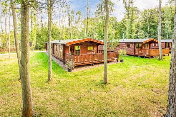 A row of wooden cabins with balconies, surrounded by a grassy area and trees.