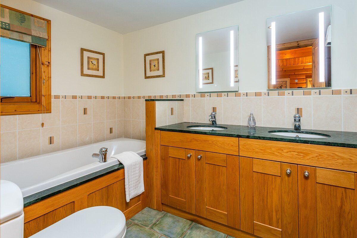 A bathroom with two sinks, a bathtub, and wooden cabinets.