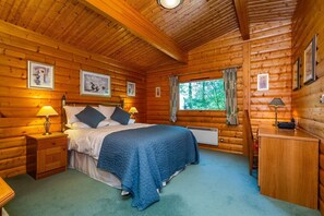 A log cabin bedroom with a bed, bedside tables, a desk, and framed pictures on the walls.