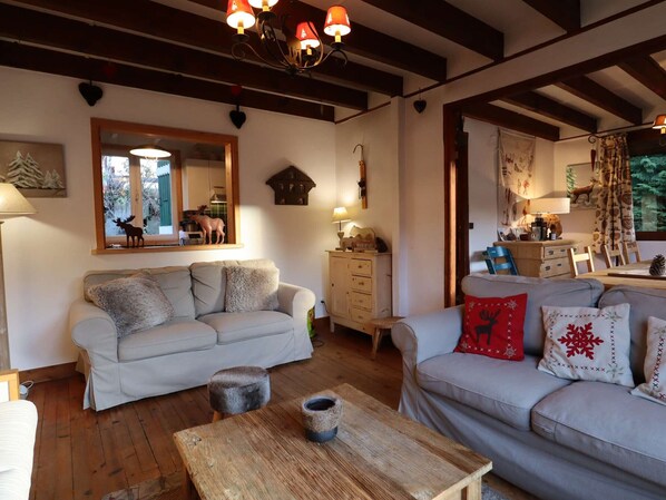 A cozy living room with two sofas, a wooden coffee table, a dresser, and a mirror reflecting a window view.