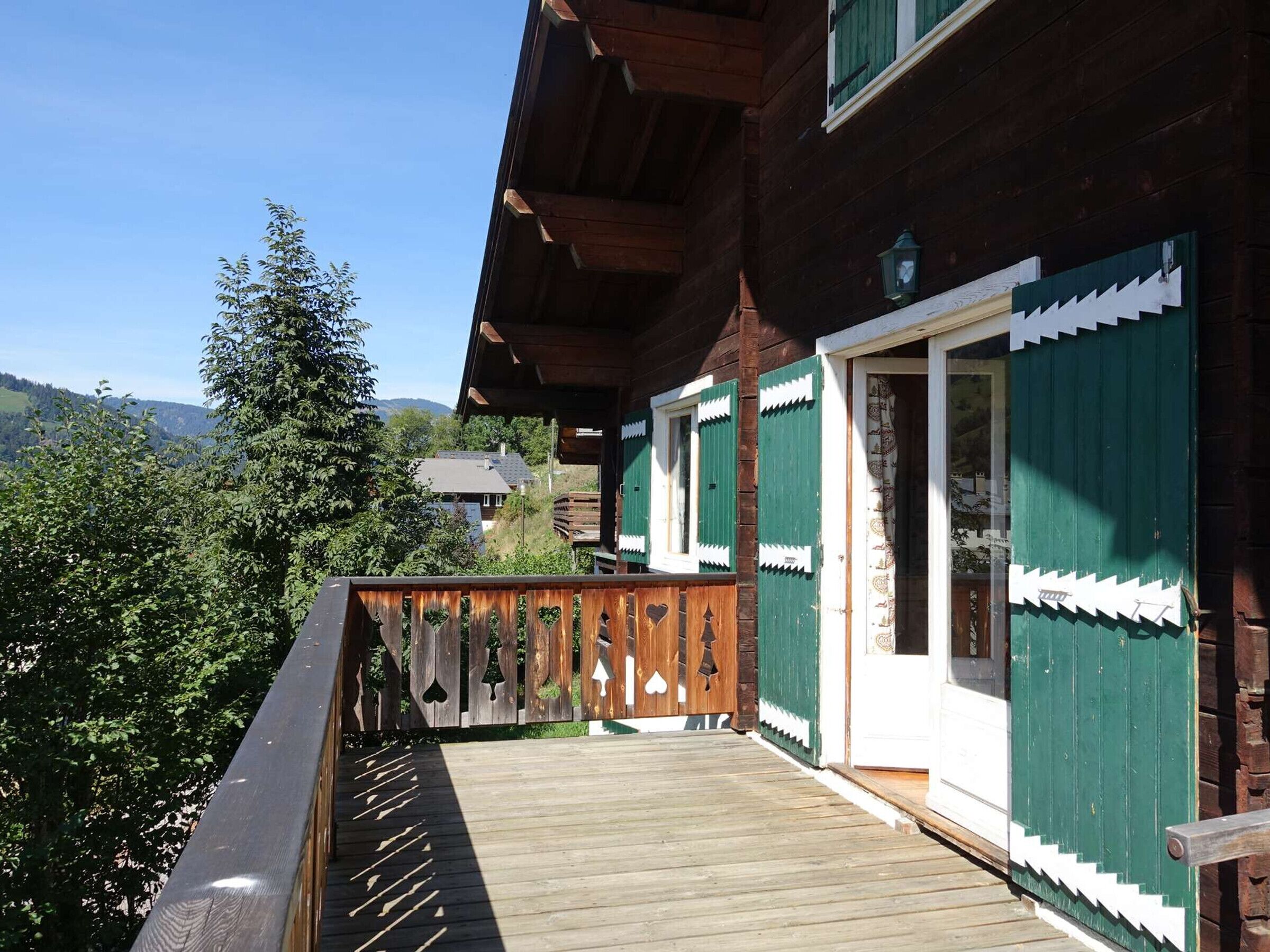 Una casa de madera con balcón, contraventanas verdes y vistas del paisaje circundante.