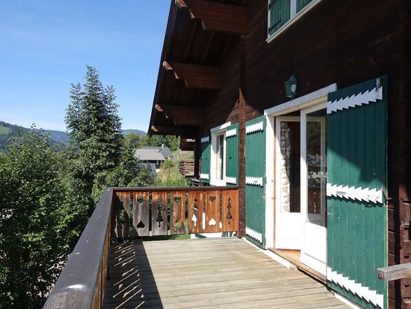 A wooden house with a balcony, green shutters, and a view of the surrounding landscape.