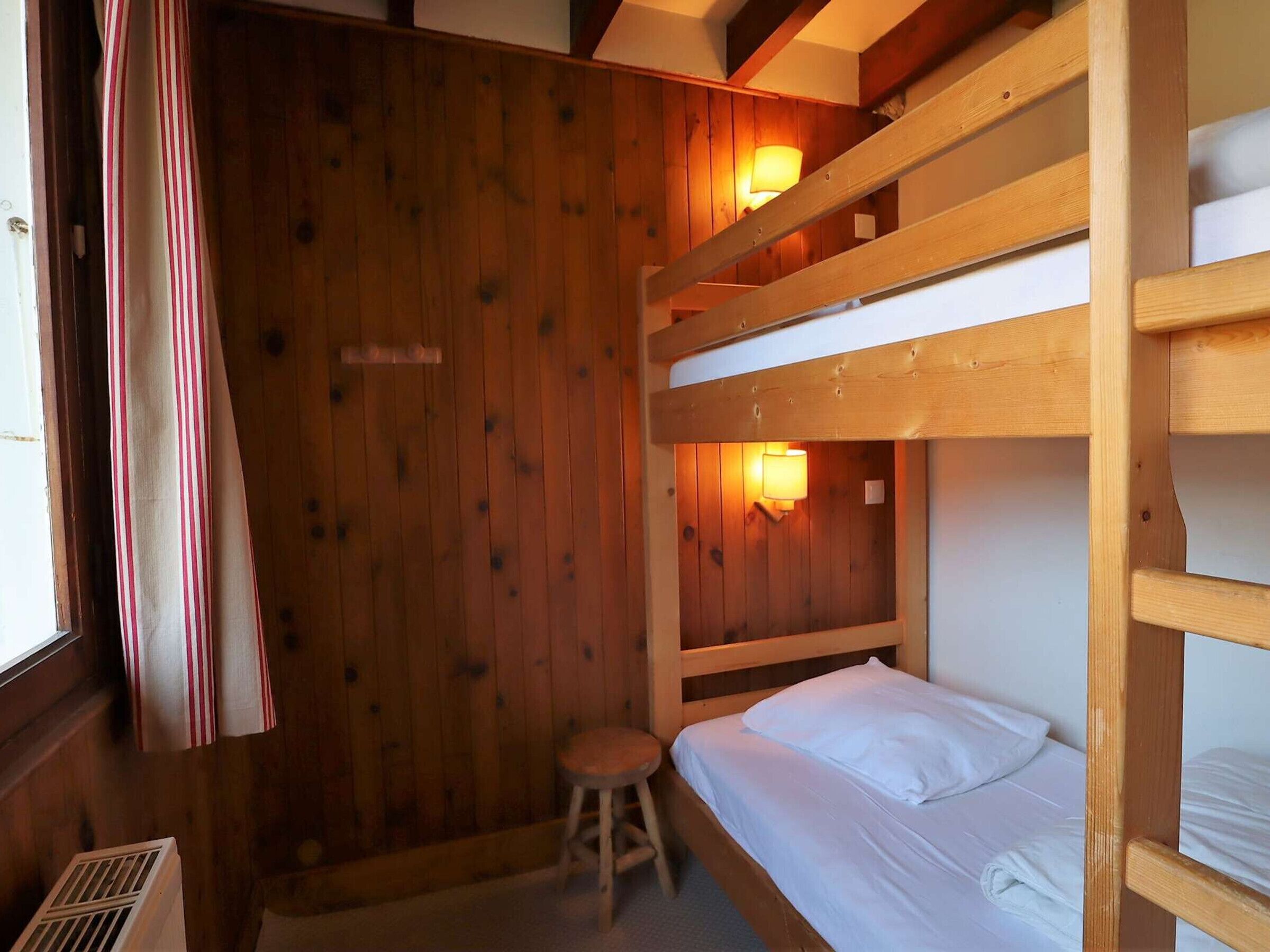 A bunk bed room with wooden walls and a window with curtains.