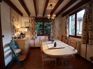 A cozy dining area with a round wooden table, chairs, a chandelier, and patterned curtains.
