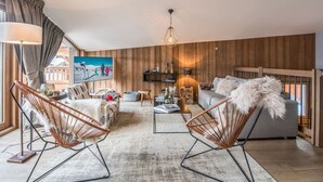Amplia sala de estar con un cuadro grande, una pared de madera, un sofá, dos sillones, una mesa de centro y un candelabro colgante.