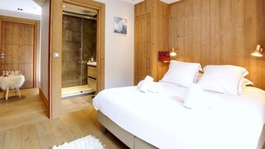 Un dormitorio con una cama grande, paredes de paneles de madera, una ducha de vidrio y una alfombra blanca y mullida.