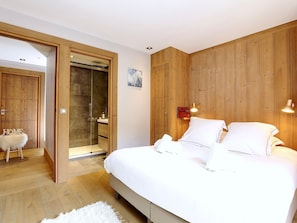Une chambre avec un grand lit, des murs recouverts de panneaux de bois, une douche en verre et un tapis blanc moelleux.
