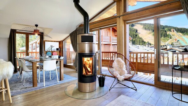 Una habitación acogedora con chimenea de leña, zona de comedor y ventanas amplias con vistas al exterior.