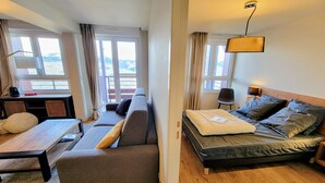 Une chambre d’hôtel moderne, dotée d’un canapé, d’un lit, d’une table en bois et offrant une vue sur l’extérieur grâce à de grandes fenêtres.