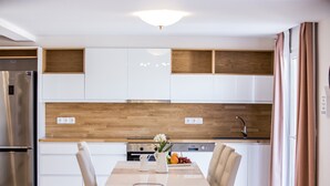 A modern kitchen with white cabinets, wooden accents, a stainless steel refrigerator, and a dining table with chairs. - Eleni Luxury Villa by White Dream Villas (Corfu)