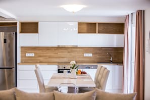 A modern kitchen with white cabinets, wooden accents, a stainless steel refrigerator, and a dining table with chairs.