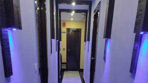 A hallway with white tiled flooring and black borders, leading to a room with a door. - Hotel OPS (Kolkata)