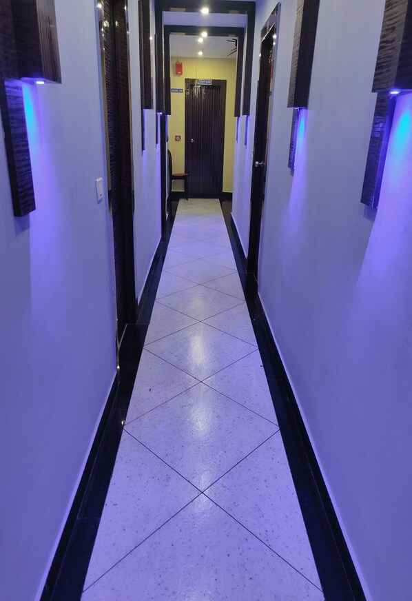 Un pasillo con suelo de baldosas blancas y bordes negros, que conduce a una habitación con una puerta.