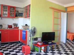 A compact room with a kitchenette, a television, and a fan.