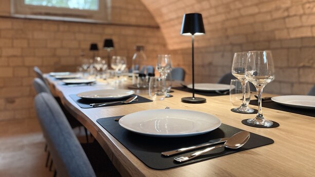 A dining table set with plates, glasses, and cutlery, in a room with brick walls and a window. - Domaine de Bonneuil (Bonneuil-les-Eaux)