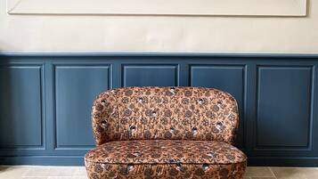 A chair with a floral pattern, a large framed artwork above it, and a blue paneled wall.