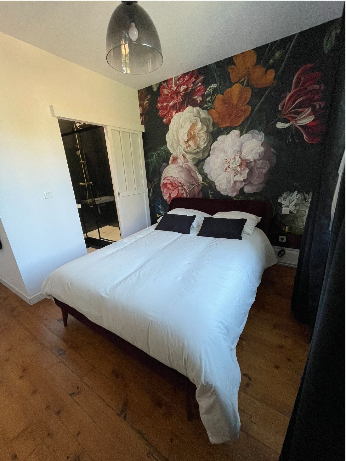 A bedroom with a large bed, a shower, and a floral mural on the wall.