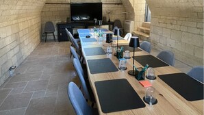 A long table with black placemats, chairs, and a television in an arched stone room. - Domaine de Bonneuil (Bonneuil-les-Eaux)