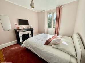 A bedroom with a bed, a dresser, a TV, and a window with curtains.