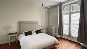 A bedroom with a large bed, a chandelier, a radiator, and a window with curtains. - Domaine de Bonneuil (Bonneuil-les-Eaux)