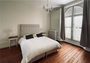 Un dormitorio con una cama grande, una araña, un radiador y una ventana con cortinas.