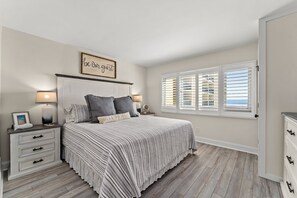 A bedroom with a bed, bedside tables, a nightstand, a window with blinds, and a wall with a sign.