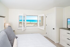 A bedroom with a bed, a nightstand, a lamp, a TV, a wardrobe, and a window with beach view.