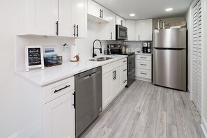 A modern kitchen with white cabinets, stainless steel appliances, and a wooden floor.