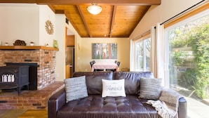 A cozy living room with a leather sofa, a brick fireplace, and a dining area visible through a glass door. - 🌲Your Home Base for Exploring the Redwoods! Pet Friendly, Complete with Hot Tub!🐾 (Mckinleyville)