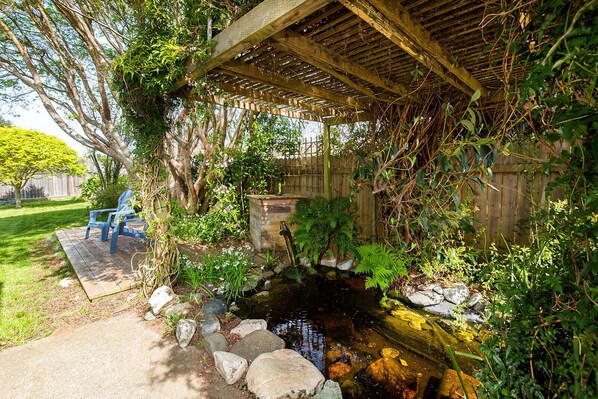 A wooden deck with chairs, a small pond, and lush greenery.