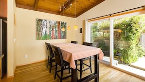 A dining area with a table, chairs, wooden ceiling, and a large window with a view of greenery. - 🌲Your Home Base for Exploring the Redwoods! Pet Friendly, Complete with Hot Tub!🐾 (Mckinleyville)