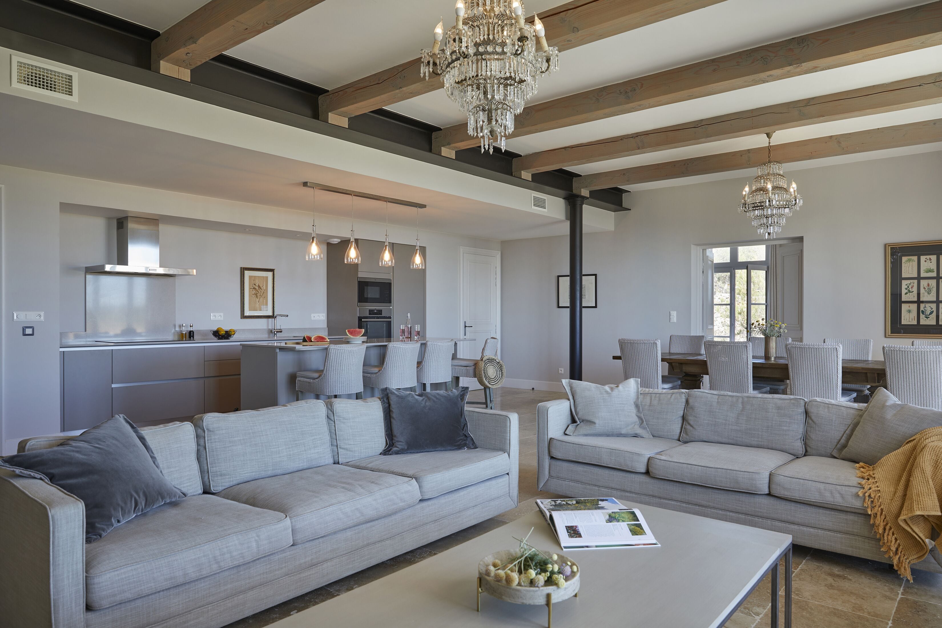 A spacious living area with a neutral color scheme, featuring two sofas, a coffee table, and a chandelier.