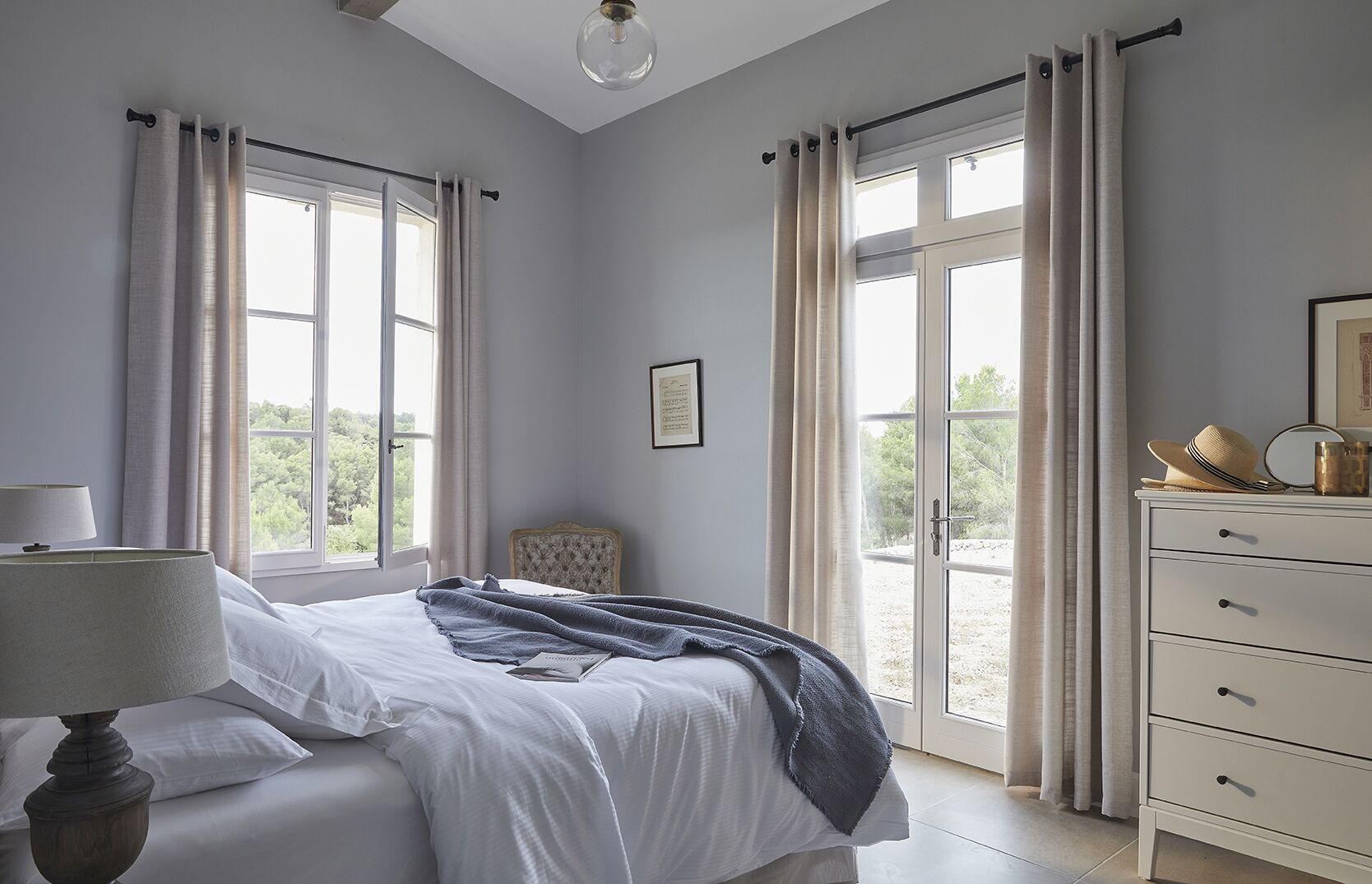 Un dormitorio con una cama, un aparador, una silla y una ventana con cortinas.