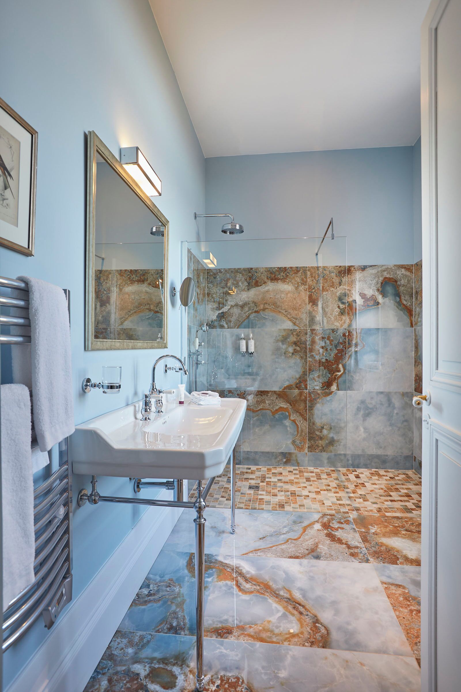 A bathroom with a marble shower wall, a white sink, and a towel rack.
