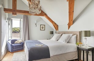 Un dormitorio con una cama grande, una silla, una mesita de noche, una lámpara de araña y vistas al exterior.