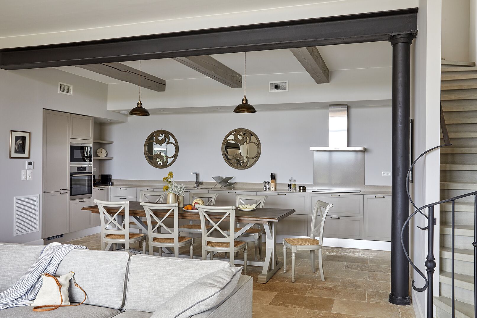 A modern kitchen with white cabinets, a dining area with white chairs, and a staircase with a black railing.