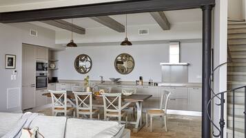 A modern kitchen with white cabinets, a dining area with white chairs, and a staircase with a black railing.