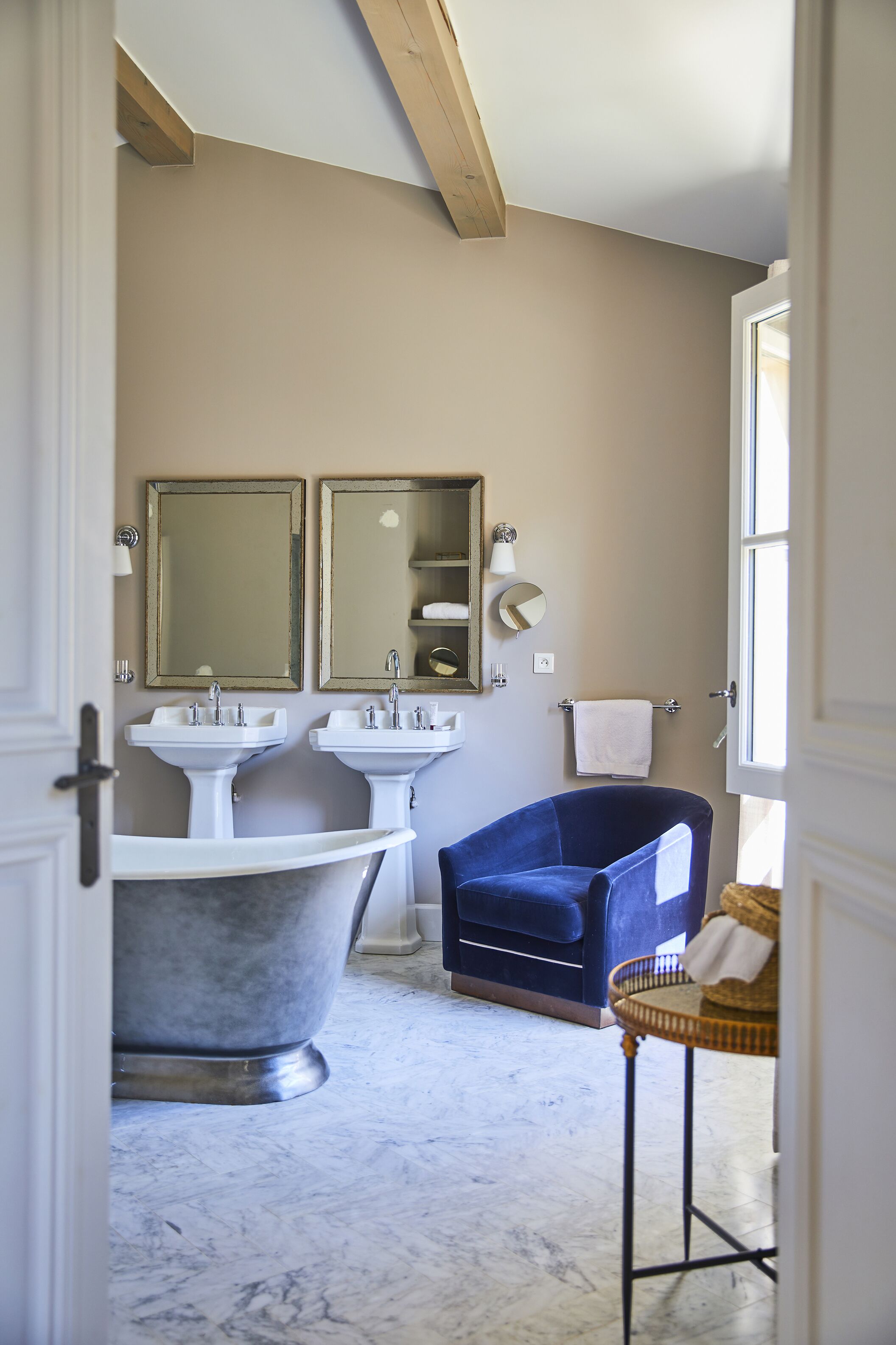 Ein Badezimmer mit zwei Waschbecken, einer Badewanne, einem blauen Stuhl und einem Korbstuhl.