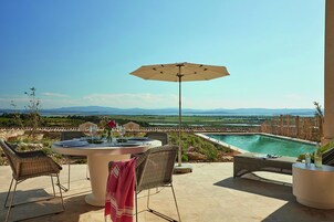 Un patio con una mesa redonda, sillas y una sombrilla con vistas a una piscina y un paisaje pintoresco.