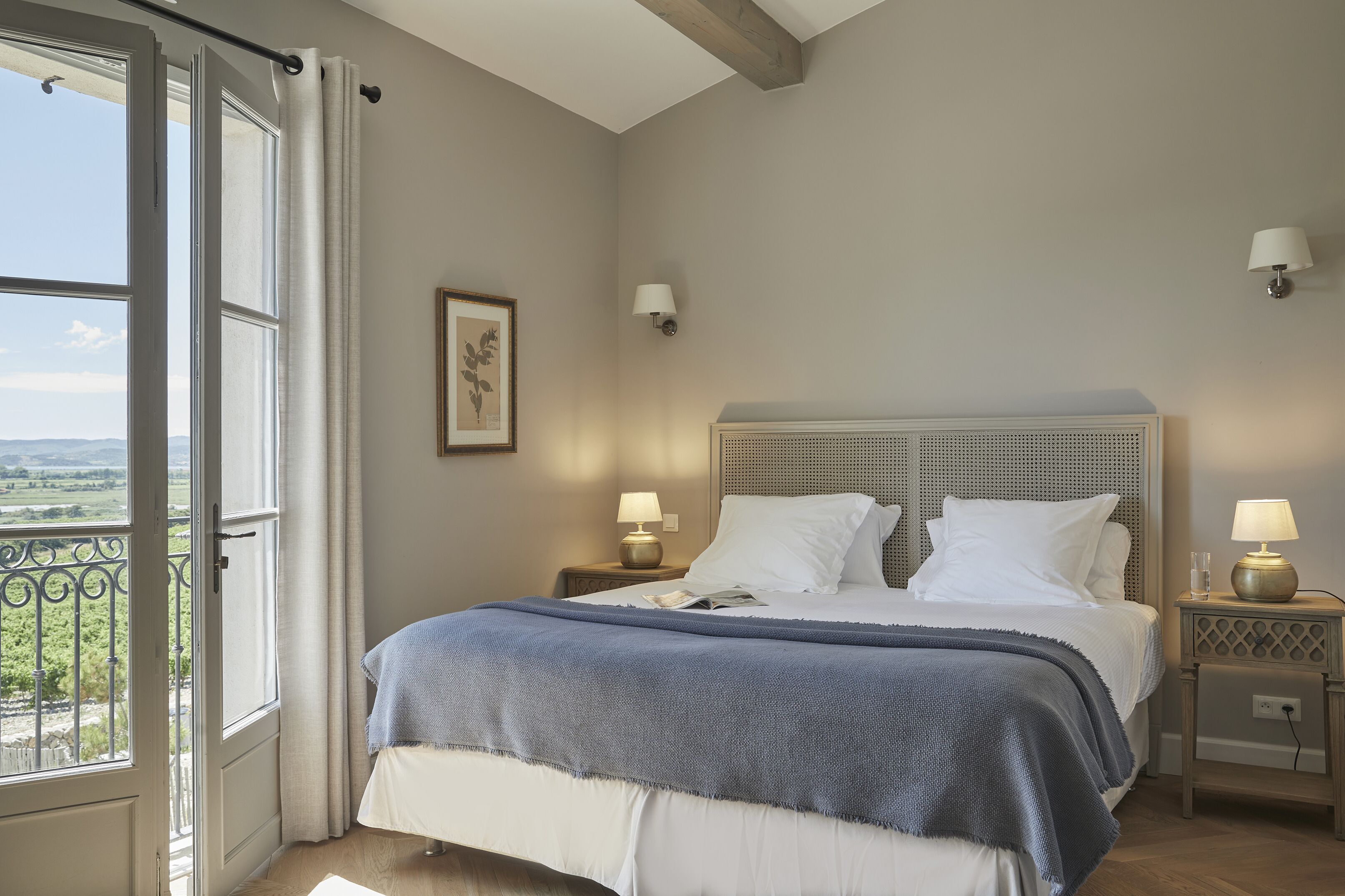 Un dormitorio con una cama grande, dos mesitas de noche con lámparas, un cuadro en la pared y vistas a través de una puerta abierta.