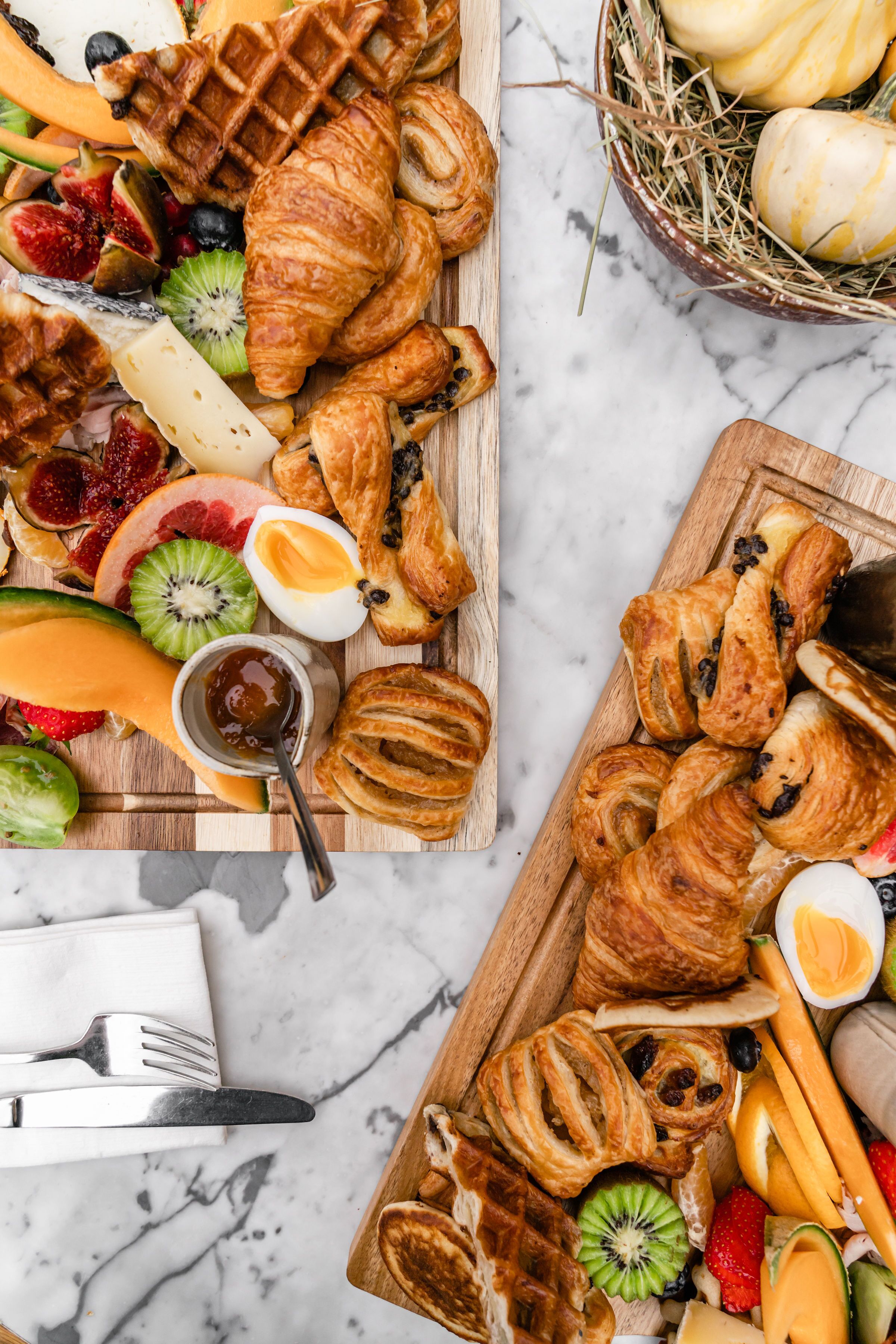 A wooden board with assorted pastries, fruits, and a small bowl of jam.