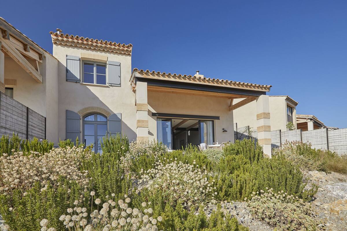 A Mediterranean-style house with a tiled roof, a covered patio, and a landscaped garden with various shrubs and plants.