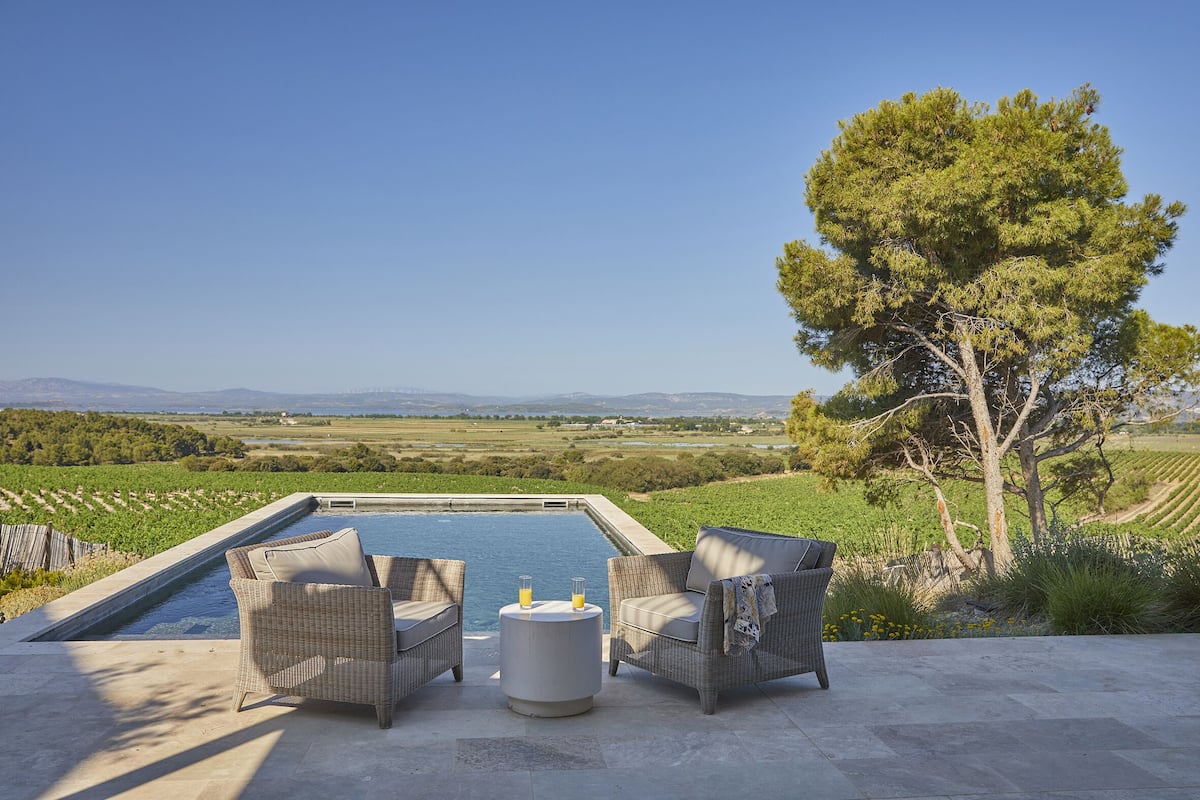 An outdoor seating area with wicker furniture and a small round table, overlooking a swimming pool and a scenic landscape.