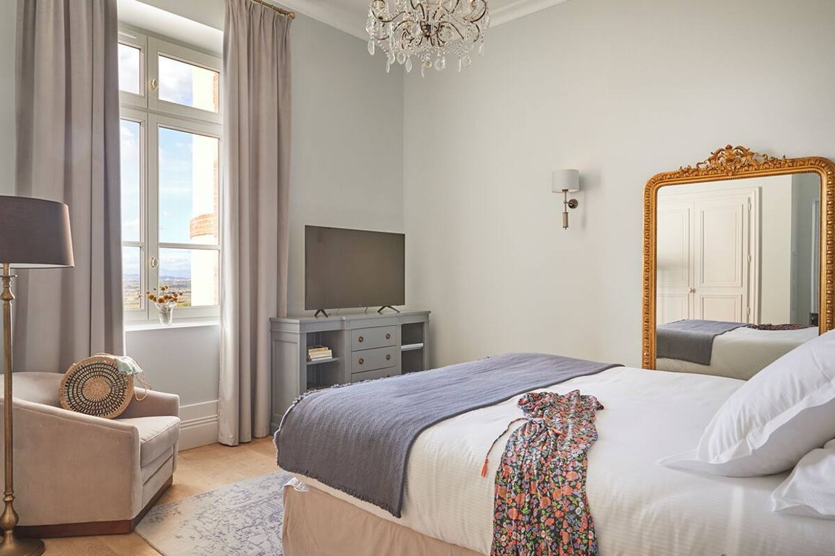 A bedroom with a bed, a dresser, a television, a chandelier, and a large mirror.