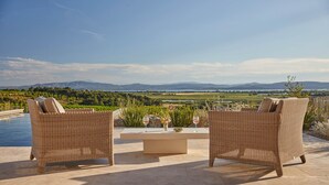 A terrace with wicker furniture and a table, overlooking a scenic landscape with mountains and a lake. - Château Capitoul (Narbonne)