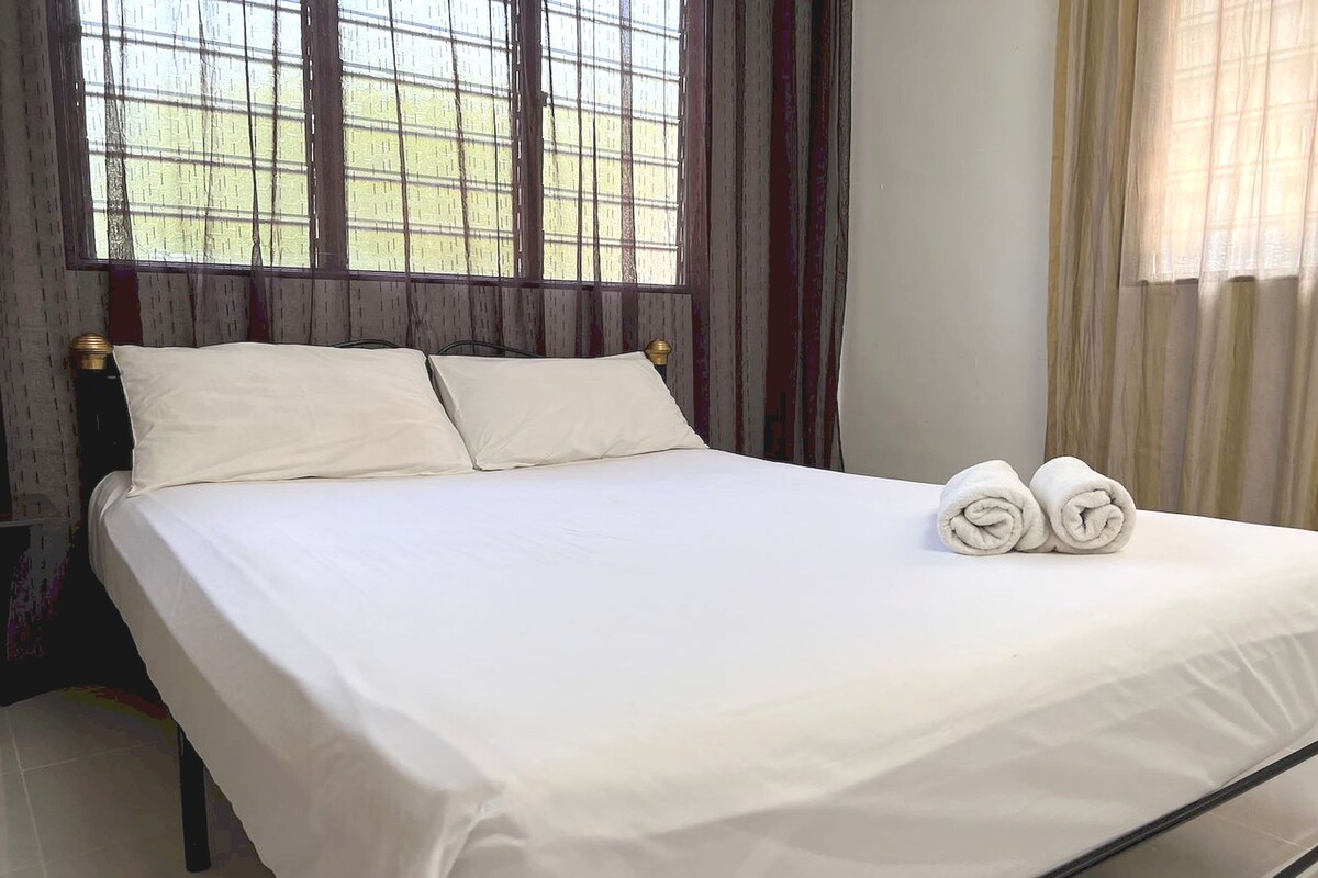 Een net opgemaakt bed met witte lakens en twee opgerolde handdoeken.
