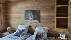 A wooden cabin bedroom with a bed, pillows, a nightstand, a lamp, a painting, and a shelf. - Chalet La Plagne Tarentaise (LA PLAGNE MONTALBERT)